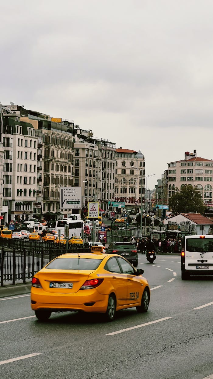 Vibrant city street with yellow taxi and bustling traffic under cloudy skies.