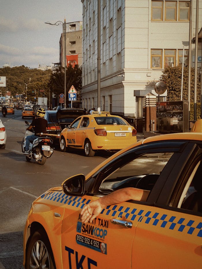 Yellow taxis and motorbikes in bustling city traffic under clear skies.
